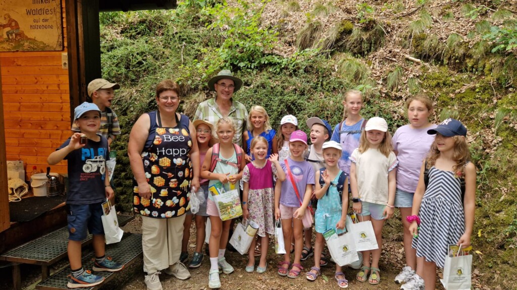 Gruppenbild von lachenden Kindern mit Betreuern vor dem Bienstand